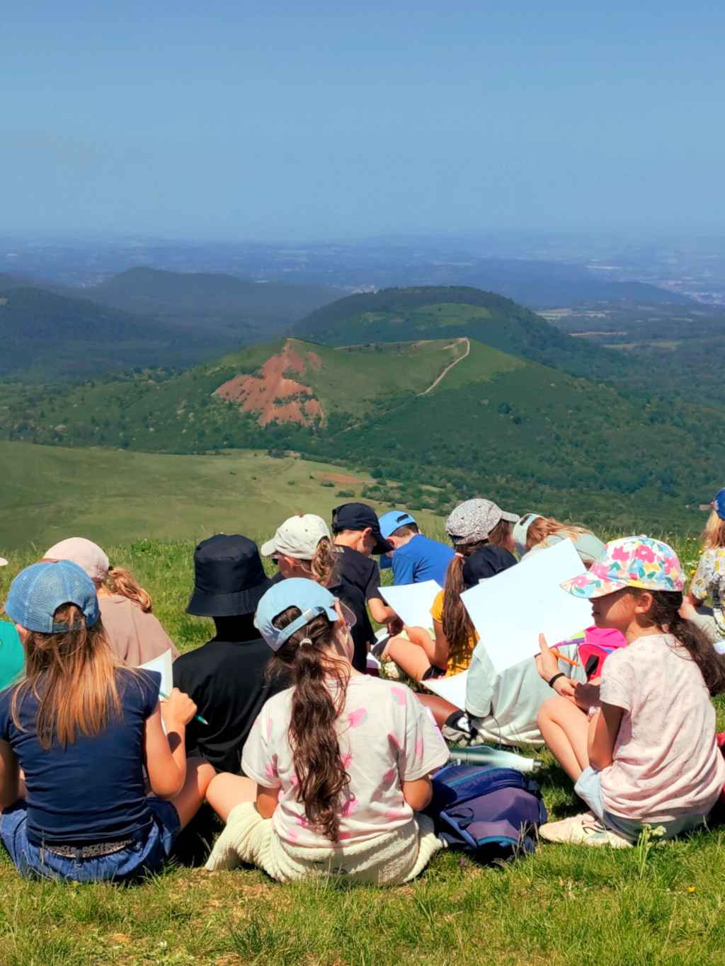 Groupe scolaire en randonnée accompagnée par Cédric Baradel sur le sommet du volcan du Puy de Dôme, massif de la Chaîne des Puys - Faille de Limagne inscrit au patrimoine mondial de l'UNESCO, Auvergne. Lecture de paysage, volcanisme auvergnat. Vue sur le Puy de Pariou.